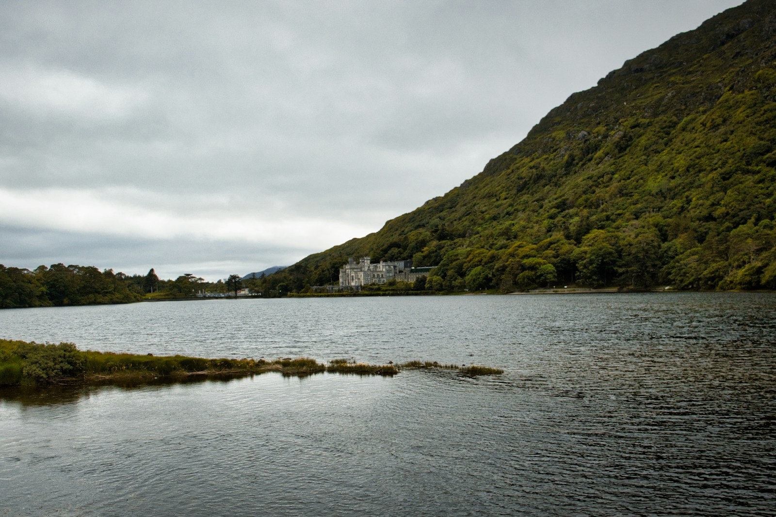 Castle nestled beside a lake and forested mountain.